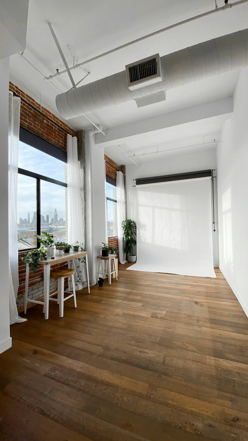Bright photo studio with white backdrop and city view windows.